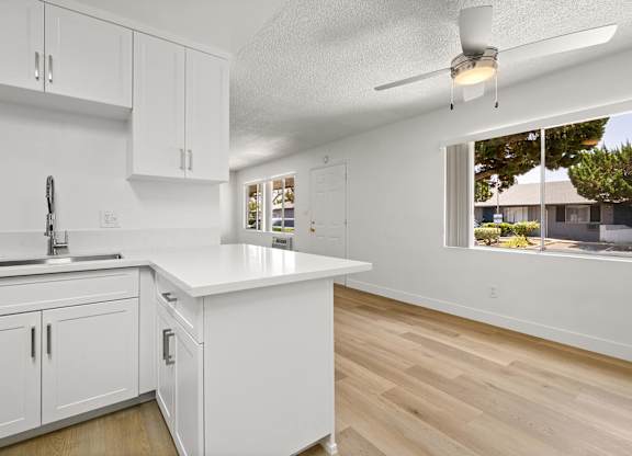 A kitchen with white cabinets and a window overlooking a backyard.