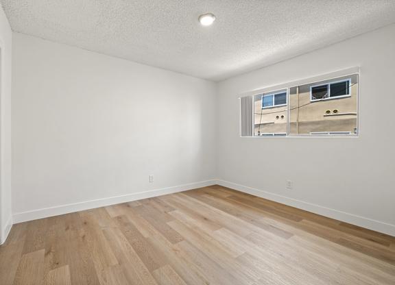A room with wooden flooring and a window showing a building outside.