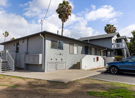 A blue car is parked in front of a house with a palm tree in the background.
