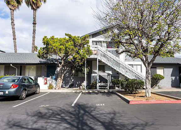 A car is parked in a parking lot in front of a building with a tree.