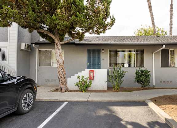 A black car is parked in front of a two-story house with a tree in front of it.