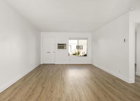 A room with a white door and a window with a view of plants outside.