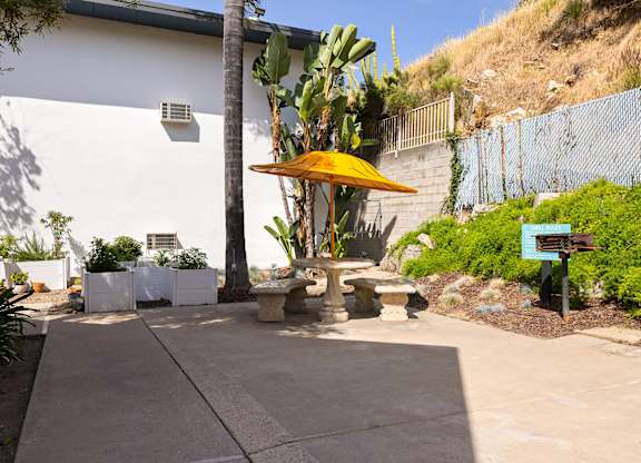 A patio area with a yellow umbrella and a white building in the background.