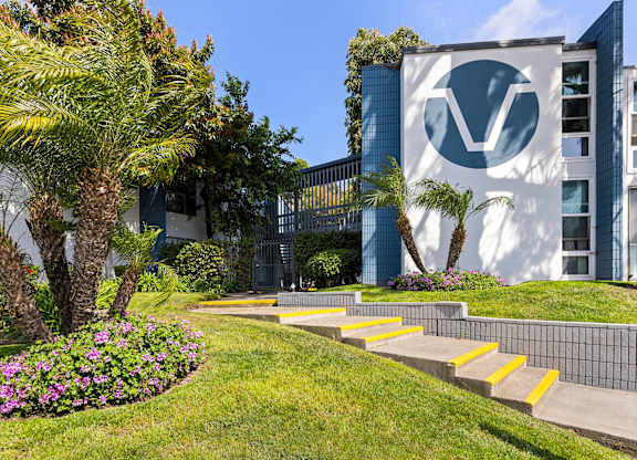 A building with a logo on it is surrounded by a green lawn and trees.