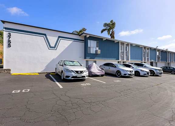 A white car is parked in a parking lot in front of a blue building.