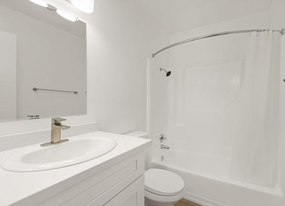 A white bathroom with a sink, toilet, and shower.