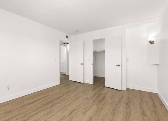 A room with white walls and wooden flooring with a door on the right.