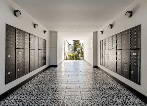 A long hallway with black and white tiles and a black wall with many mailboxes.