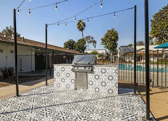 A black and white tiled outdoor kitchen area with a grill and a pool in the background.
