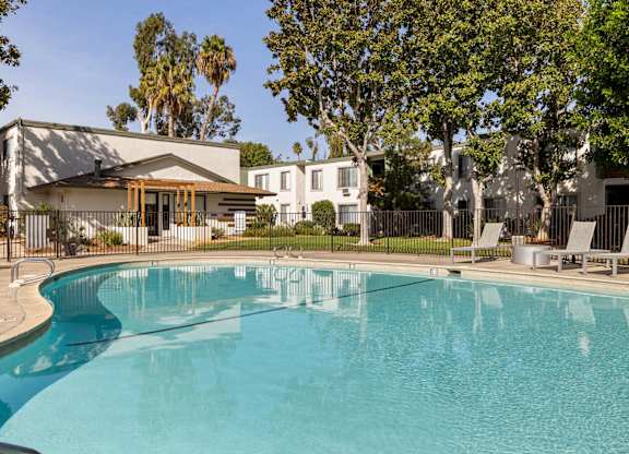 A swimming pool in front of a house with trees in the background.