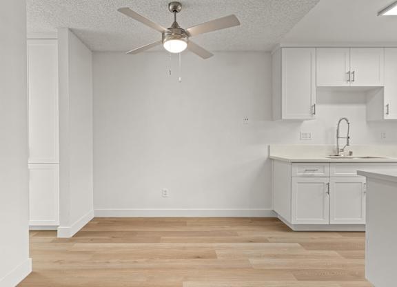 A white kitchen with a ceiling fan and wooden floors.