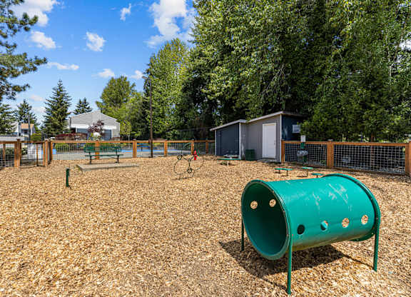 A playground with a green tube slide and a brown wooden fence.