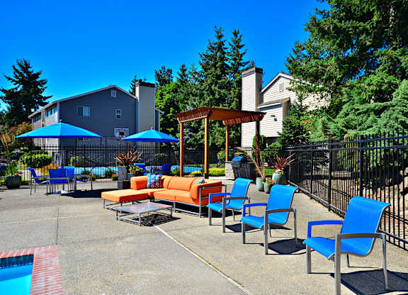 A poolside area with blue chairs and a wooden pergola.