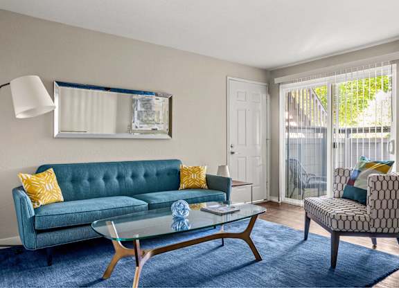 A living room with a blue couch and a glass coffee table.
