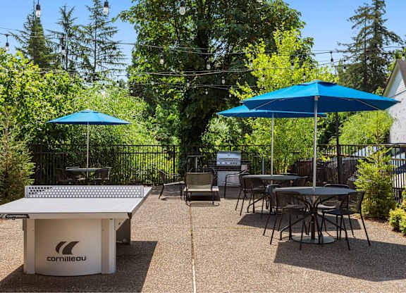 A cornilleau table tennis table is surrounded by chairs and umbrellas in a backyard setting.