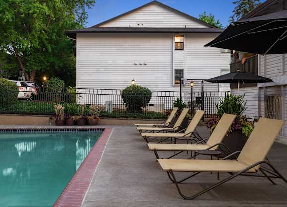 A pool with chairs and a house in the background.