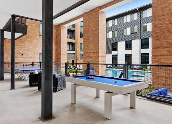A pool table is surrounded by a black railing in a room with brick walls.