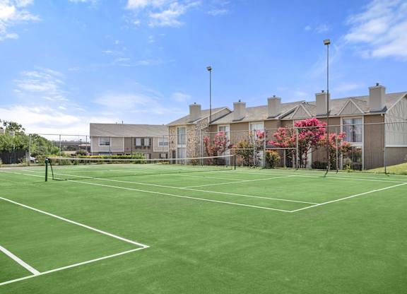 A tennis court is surrounded by apartment buildings.
