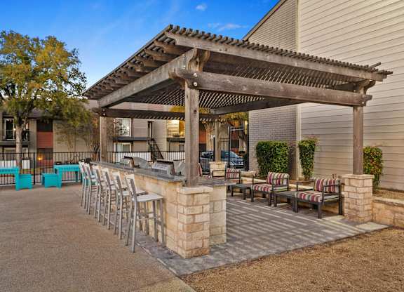 A patio with a pergola and chairs is set up outside a house.