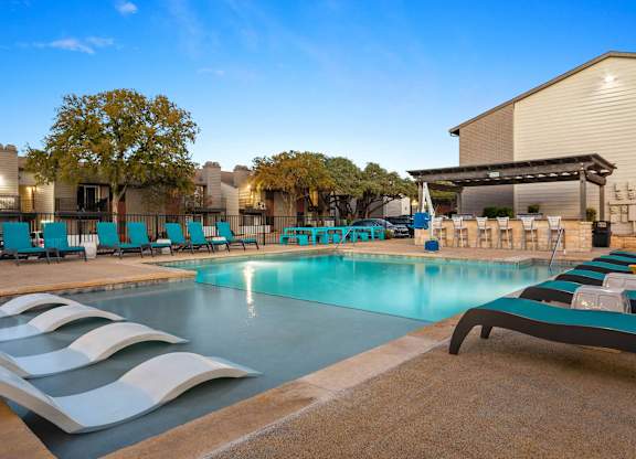 A swimming pool with sun loungers and a building in the background.