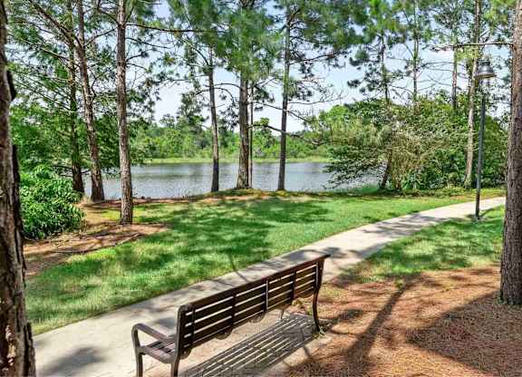 A park bench is situated on a concrete path next to a tree and a lake.
