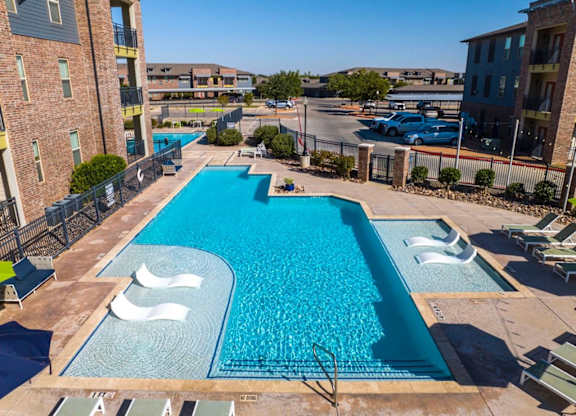 A large swimming pool surrounded by a fence and lounge chairs.