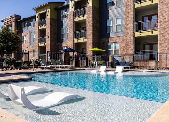 A pool surrounded by white chairs and a building in the background.