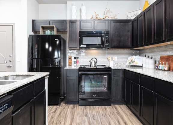A black fridge and oven in a kitchen with wooden floors.