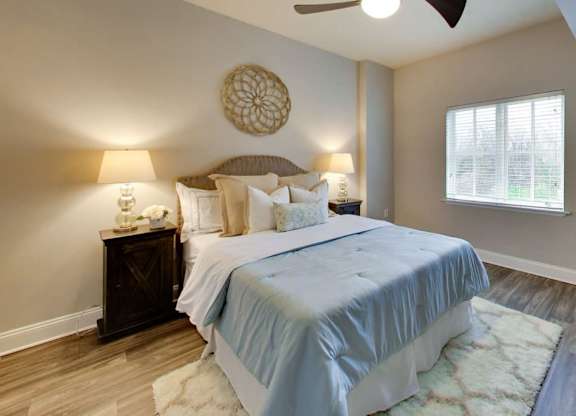 A bedroom with a bed, two lamps, a ceiling fan, and a window.