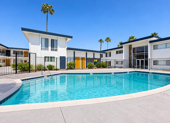 A swimming pool in front of a building with a palm tree.