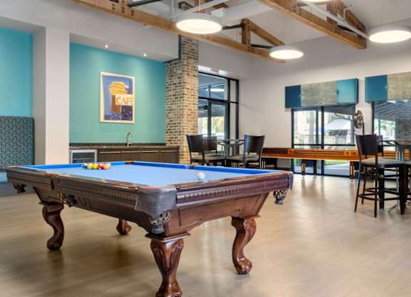 A pool table is in the middle of a room with a brick pillar and a blue wall.