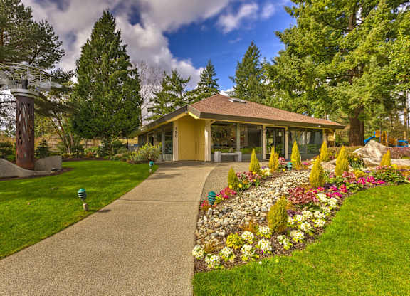 A yellow building with a brown roof is surrounded by a garden with a variety of flowers.