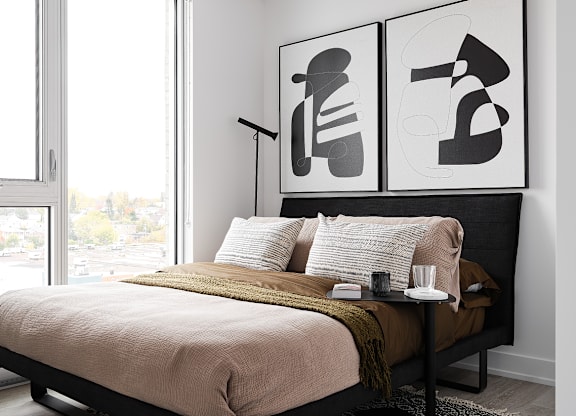 A bedroom with a bed, a table with a glass, a candle, and a plate, and two posters on the wall.