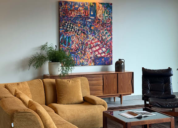 A living room with a yellow couch and a large painting on the wall.