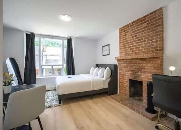 A bedroom with a brick fireplace and a bed with white pillows.