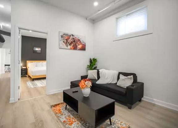 A living room with a black couch, a coffee table, and a painting on the wall.