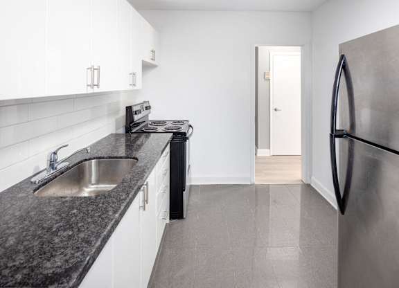 A modern kitchen with a stainless steel refrigerator and black granite countertops.