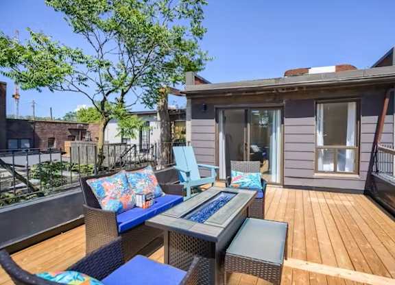 A patio with a table and chairs is surrounded by a deck and a tree.