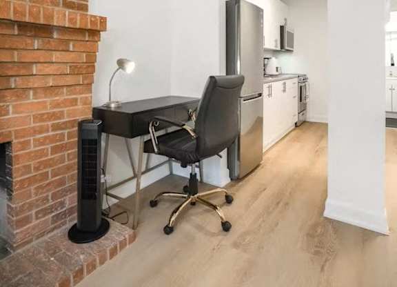 A black chair is in front of a black desk with a lamp on it.