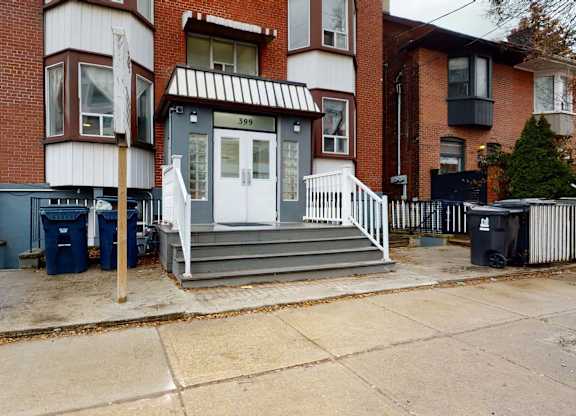A house with a white door and a black trash can in front of it.