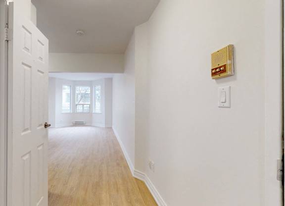 A white hallway with a wooden floor and a white door.