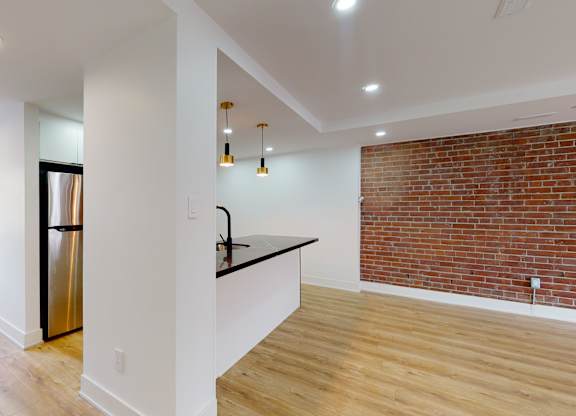 A kitchen with a refrigerator, sink, and a counter with a brick wall in the background.