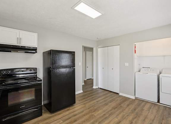A black refrigerator stands in a kitchen with a stove, dishwasher, and washing machine.