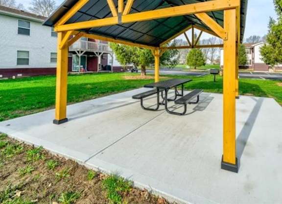 A covered picnic table with a yellow frame is situated in a grassy area at Ridgeview Apartments, Fortville, IN, 46060