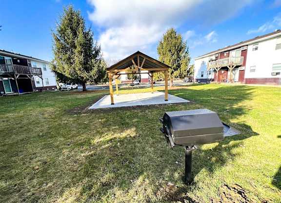 A covered picnic area with a grill in the foreground and apartment buildings in the background at Ridgeview Apartments, Fortville 46060