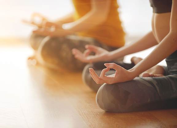 Two people are sitting cross-legged on the floor in a meditative pose.