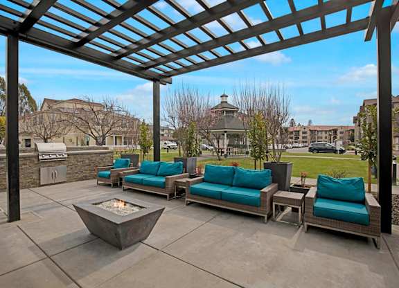 A patio with a fire pit and couches under a pergola.