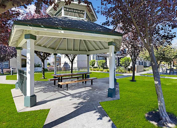 A gazebo with a bench is surrounded by a green lawn.