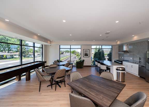 A modern community room kitchen with a dining table, comfortable chairs and shuffle board game.