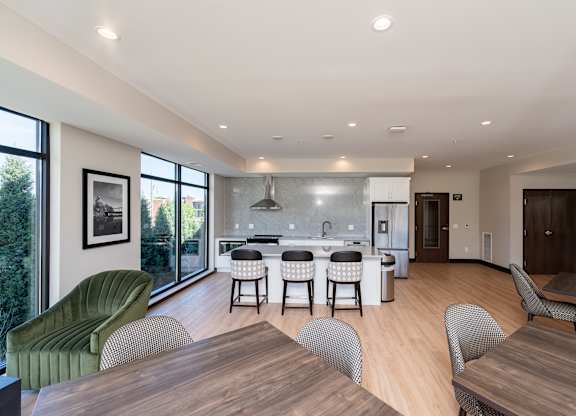 A modern community room kitchen with a dining table, comfortable chairs and shuffle board game.
